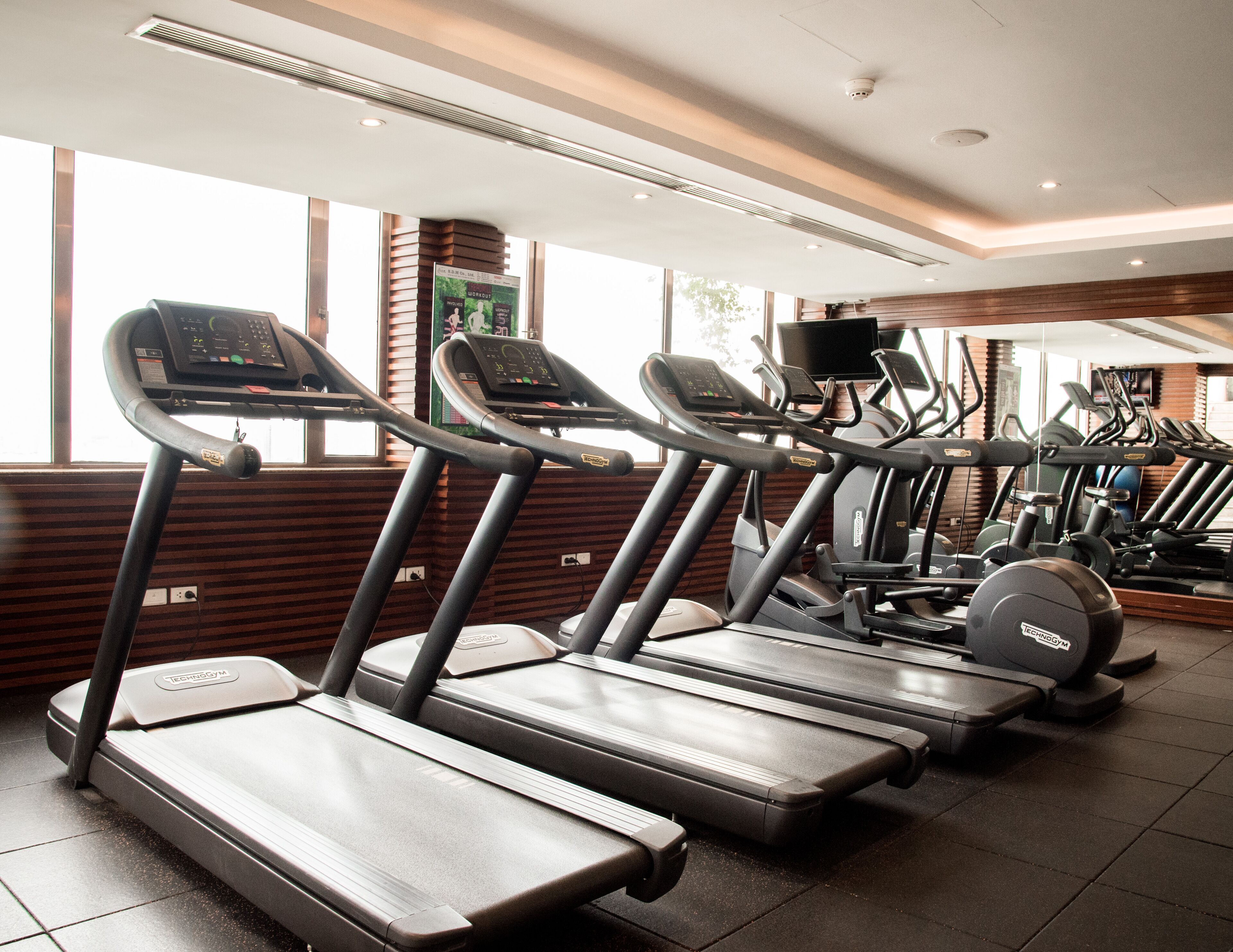 A gym with multiple treadmills, exercise bikes, and a television screen.