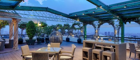 An outdoor patio with wicker furniture, a glass-top table, and potted plants.