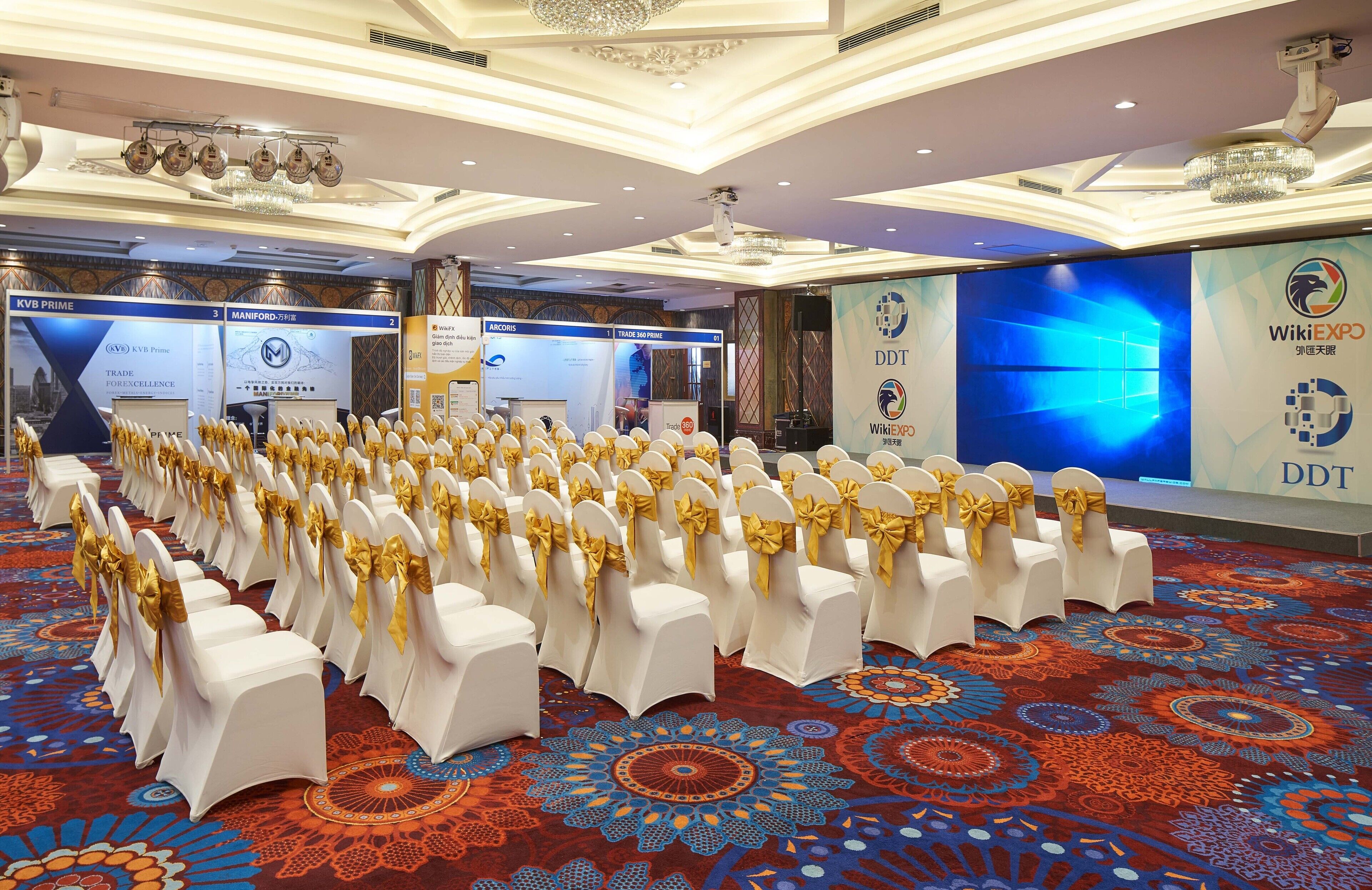 A conference room with rows of white chairs with gold sashes, a patterned carpet, and banners for KVB Prime and WikiEXP.
