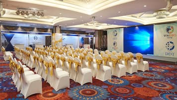 A conference room with rows of white chairs with gold sashes, a patterned carpet, and banners for KVB Prime and WikiEXP.