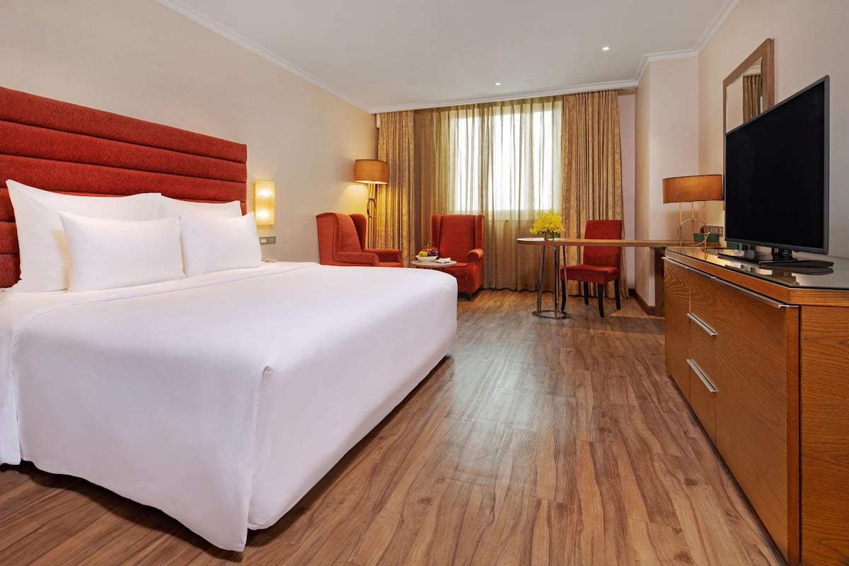 Une chambre d’hôtel avec un grand lit, une commode en bois, un téléviseur et deux chaises.