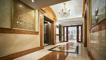 A luxurious hallway with marble flooring, ornate wall panels, and a grand chandelier.