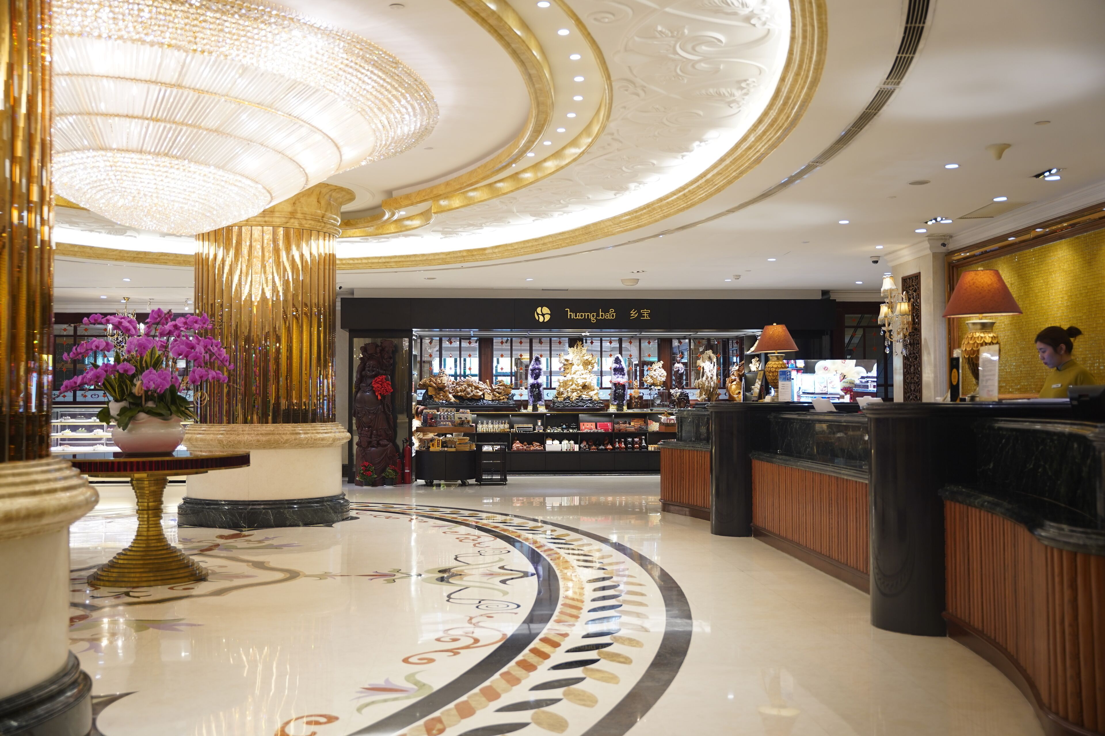 A luxurious lobby with a grand chandelier, a reception desk, and a display of luxury items.