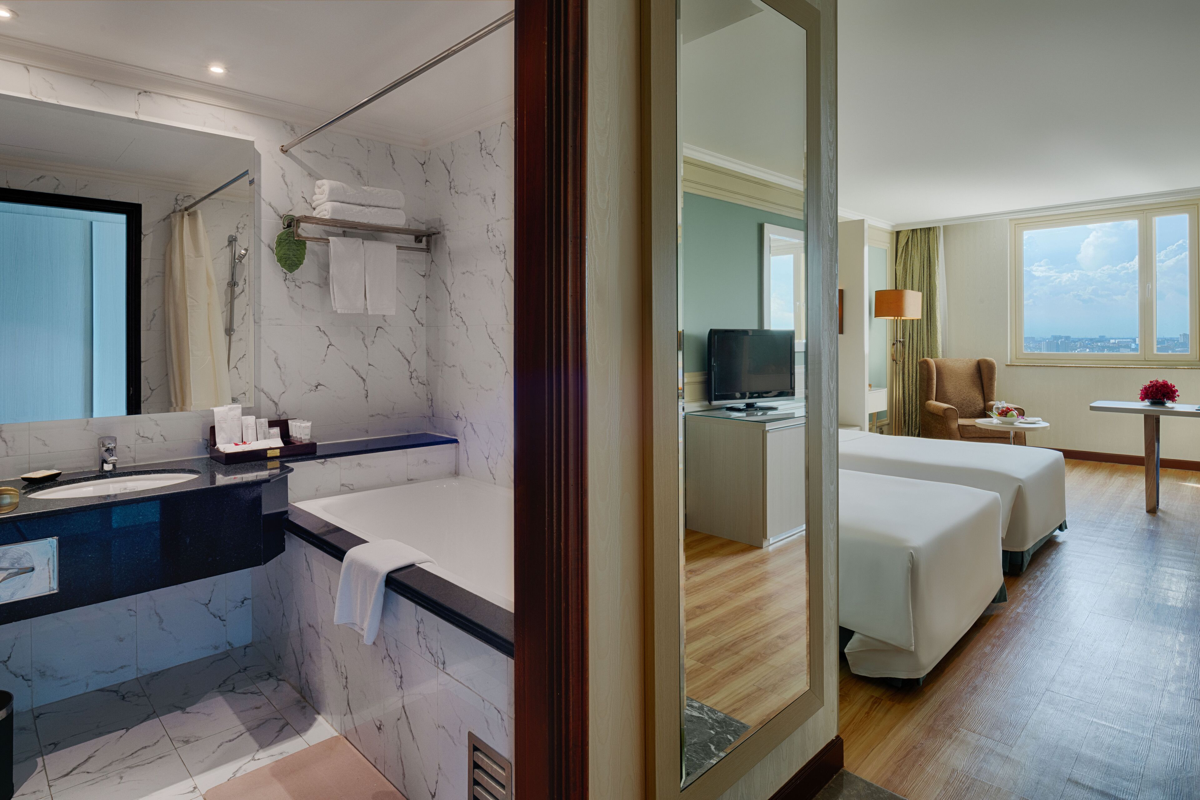 Habitación de hotel con baño de mármol, televisor, escritorio y dos camas.