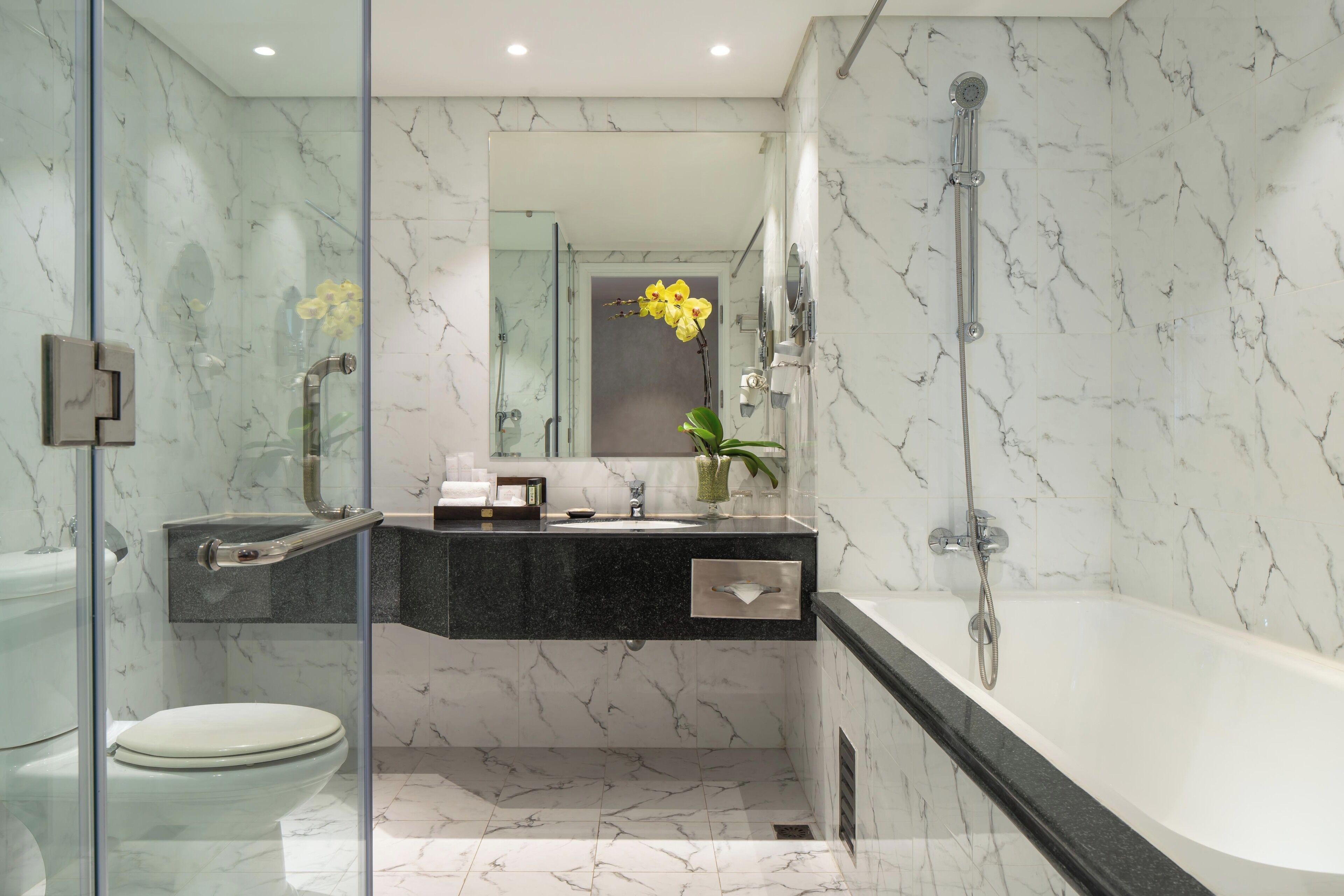 A modern bathroom with a glass shower enclosure, a white bathtub, and a marble-tiled floor.