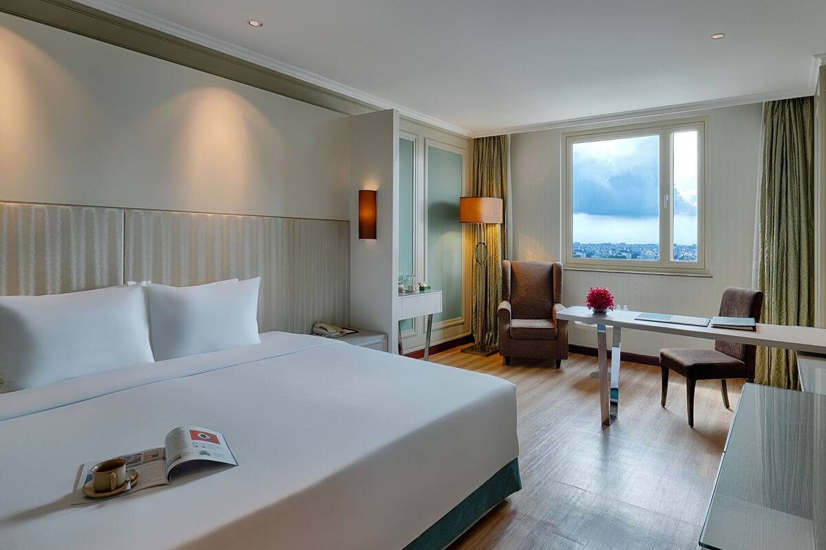 Une chambre d’hôtel avec un grand lit, un bureau, une chaise, une lampe et une vue sur la ville.