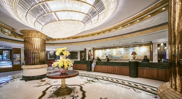 A luxurious lobby with a grand chandelier, a reception desk, and a decorative floor pattern.