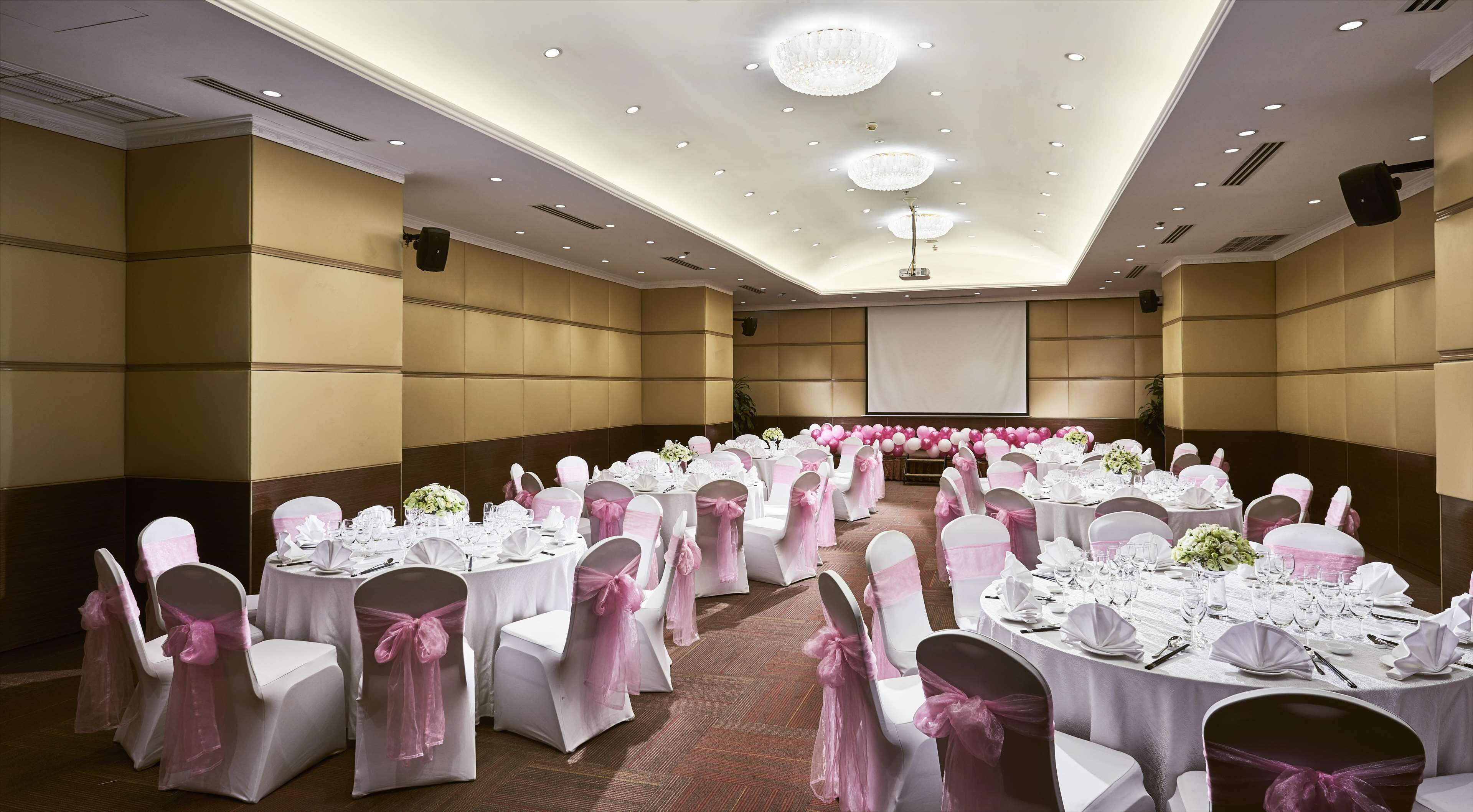 A banquet hall with round tables, white chairs, and pink sashes.