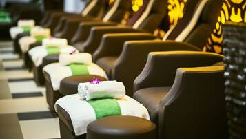 A row of massage chairs with towels and green headrests, arranged in a spa setting.