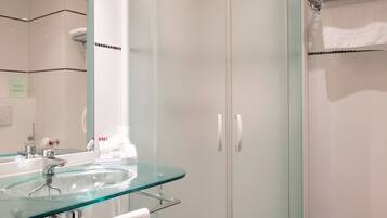 A modern bathroom with a glass-enclosed shower, a glass sink, and a white towel rack.