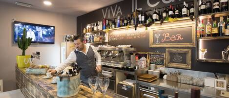 A bar area with a counter, wine bottles, glasses, and a TV screen.