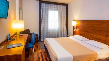 A hotel room with a bed, desk, chair, and a TV on the wall.