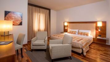 A hotel room with a bed, two armchairs, a desk, a lamp, and a painting on the wall.