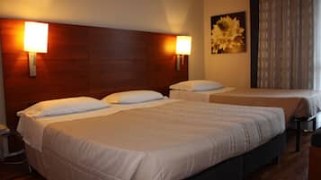 Une chambre d’hôtel avec trois lits, chacun doté de draps blancs et d’une tête de lit. Des lampes murales sont fixées de chaque côté des lits.