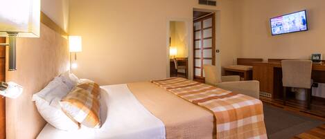 Habitación de hotel con cama, escritorio, silla, televisión y baño.