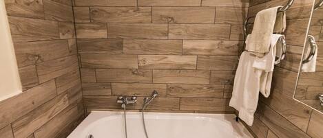 Un baño con pared de madera, una bañera, un inodoro y un perchero para toallas.