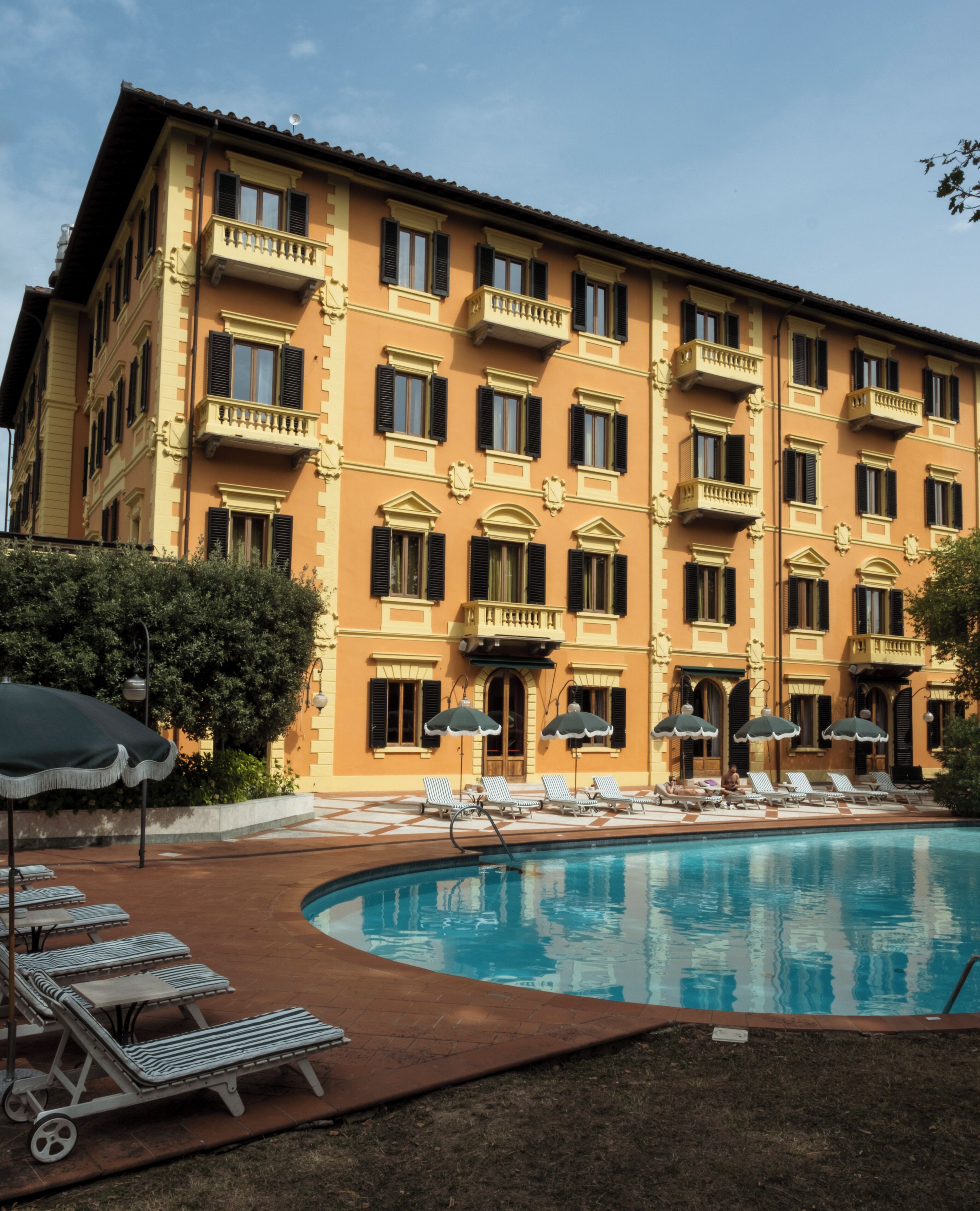 A large building with multiple balconies, a swimming pool with lounge chairs, and umbrellas.