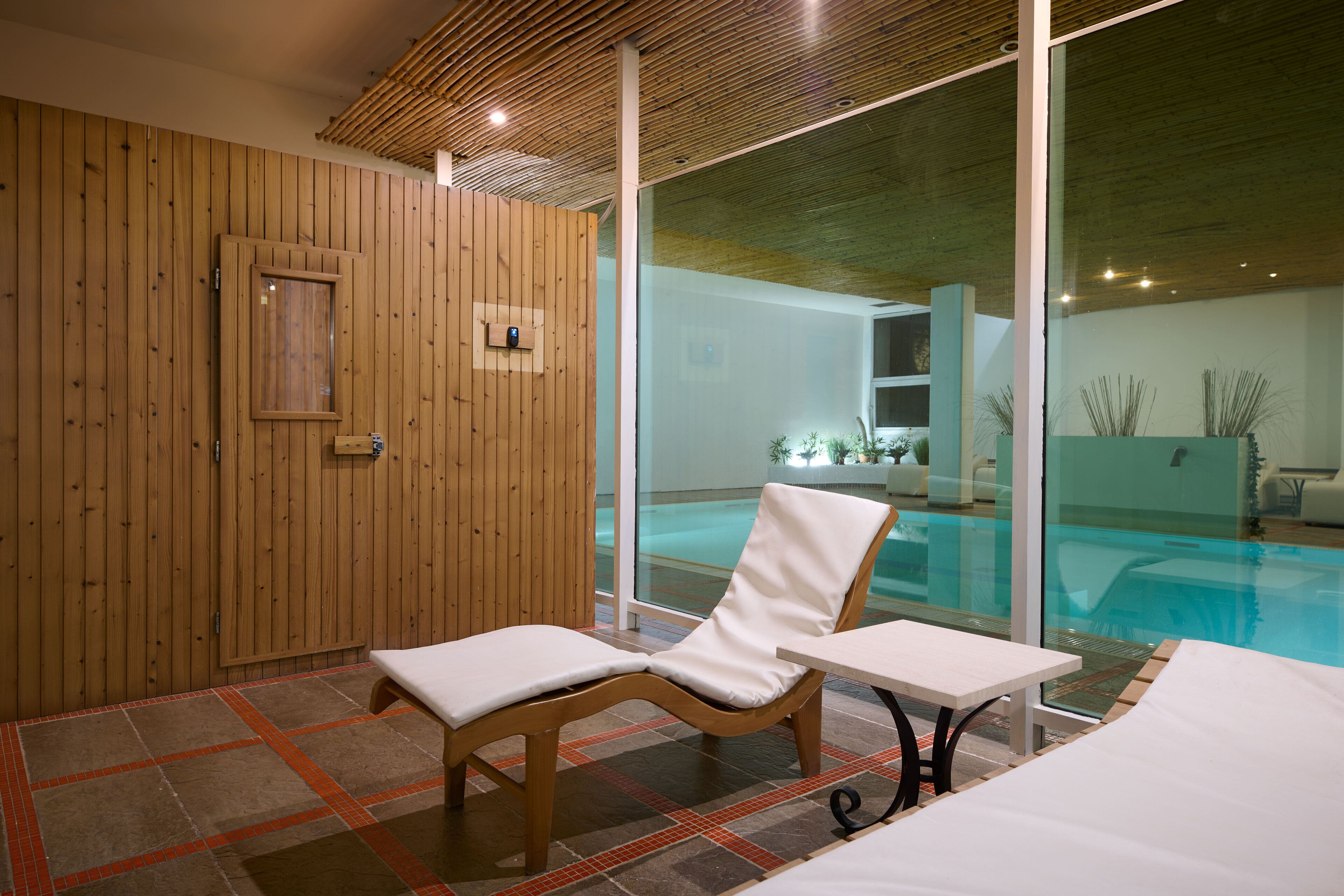 A spa room with wooden walls, a glass door leading to a pool, and two lounge chairs.