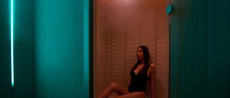 A woman sitting in a room with a tiled wall and a glass door.