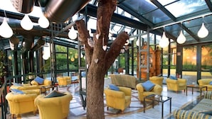Un espace intérieur moderne avec des fauteuils jaunes, un arbre central et un plafond en verre.