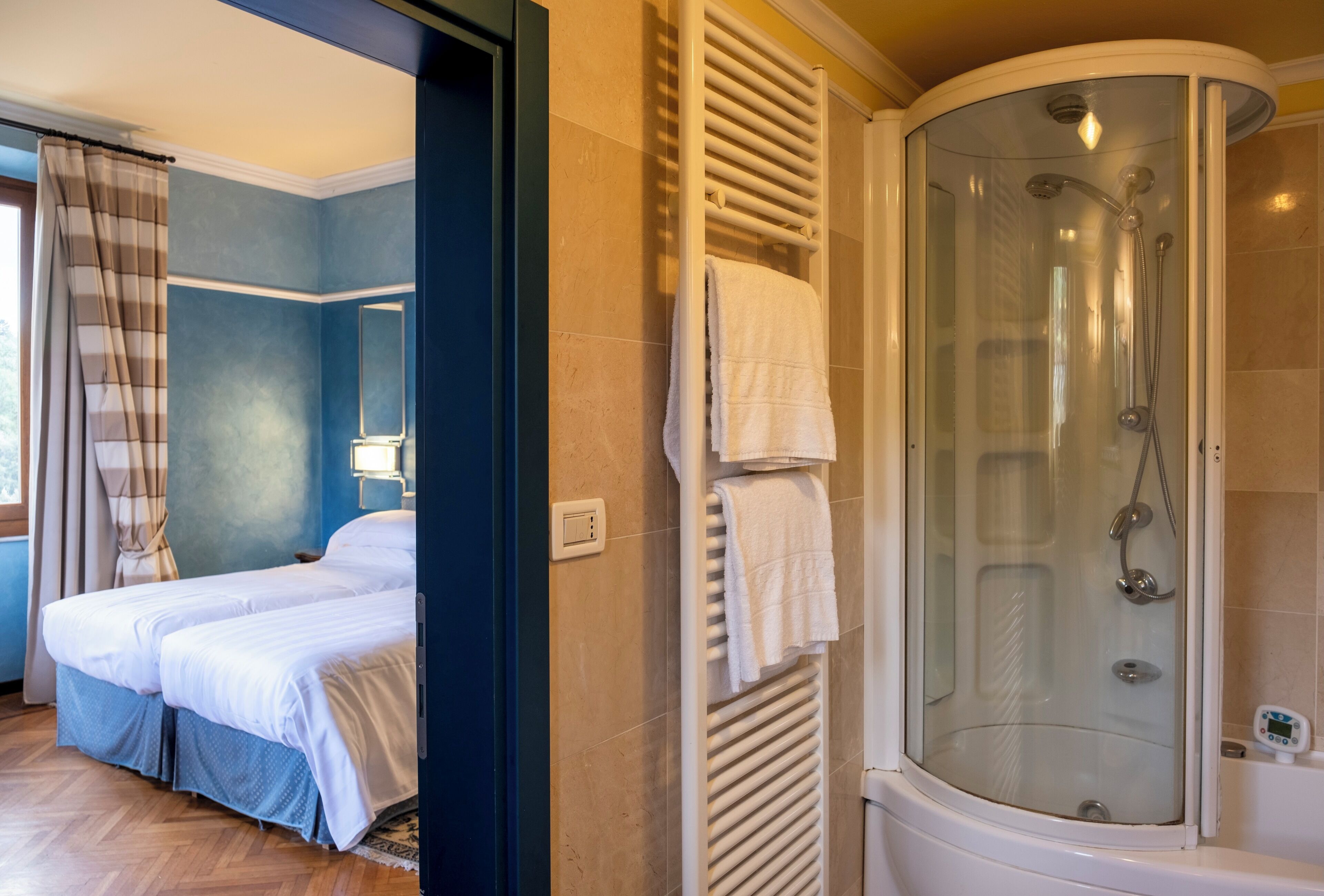 A hotel room with a bed, a glass-enclosed shower, and a bathroom with a bathtub.