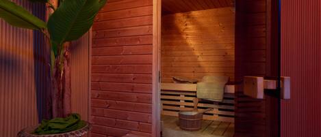 A wooden sauna with a bench, a small table, and a decorative plant.