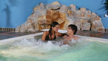 Um casal em uma banheira de hidromassagem com paisagem rochosa ao fundo.