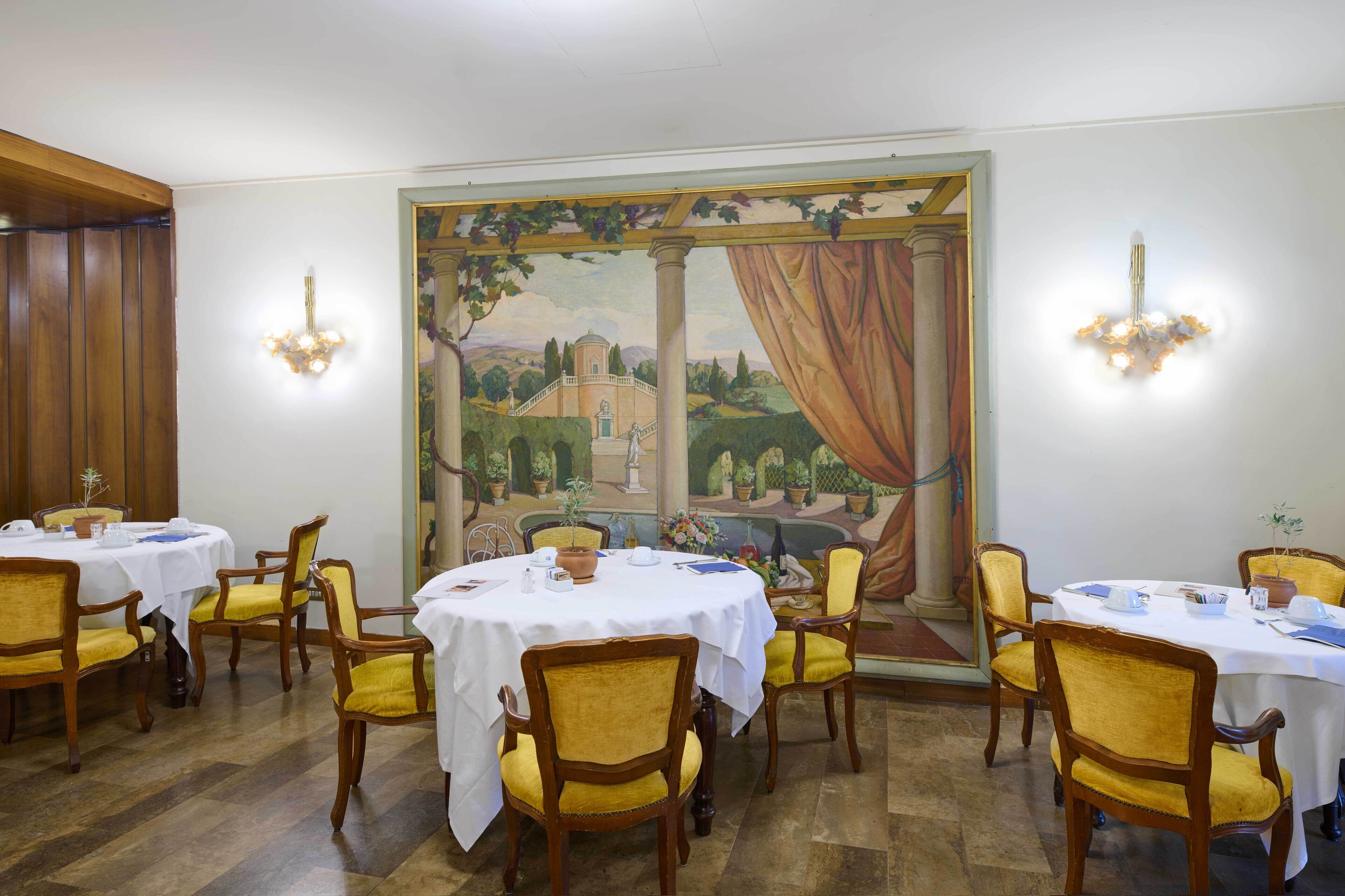 A dining area with round tables, yellow chairs, and a mural of a landscape with columns and a building.
