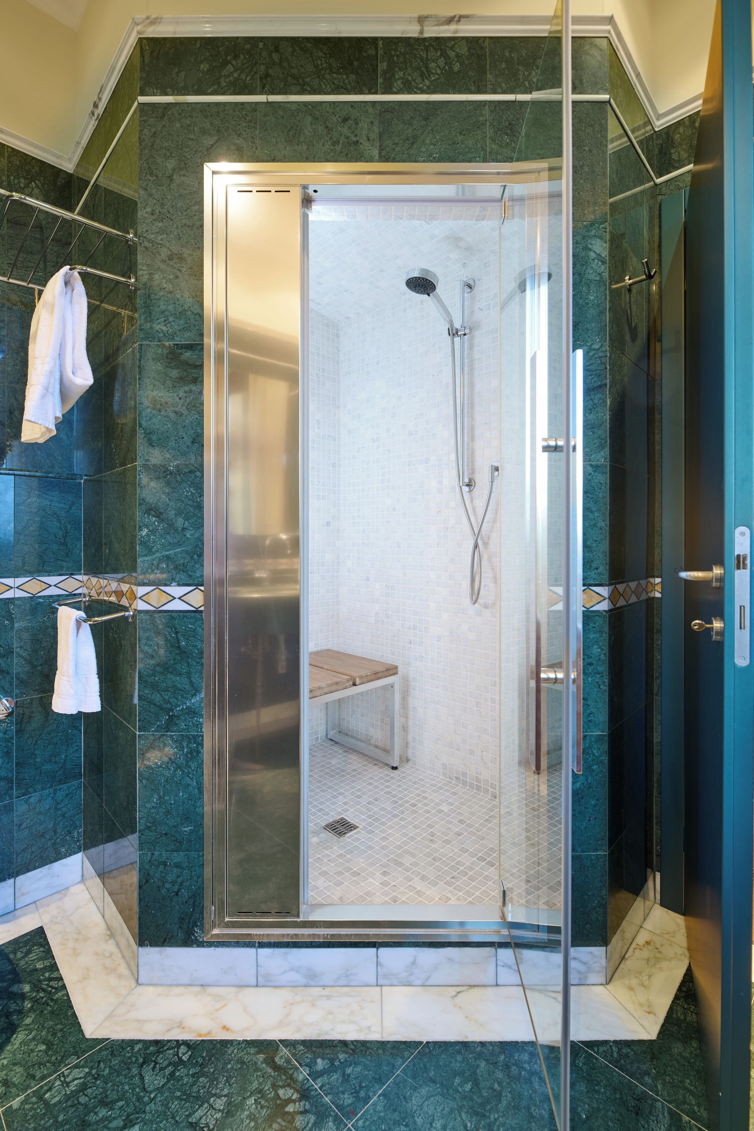 Eine begehbare Glasdusche mit Sitzbank, Marmorwänden und einem Handtuchhalter.