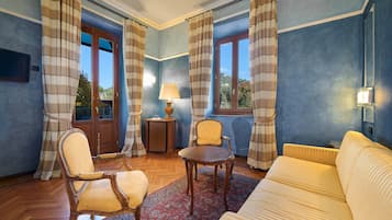 Una habitación con un sofá, dos sillas, una mesita, una lámpara y vistas al exterior a través de una ventana.
