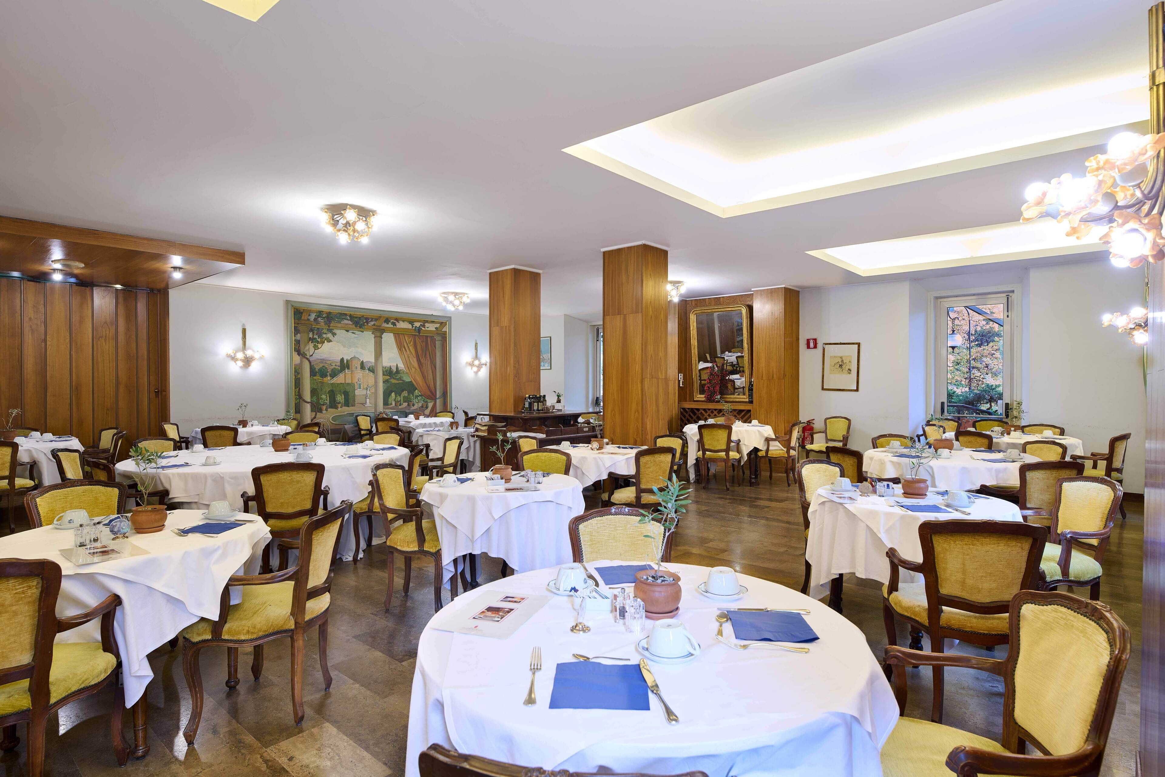 A dining area with round tables set for service, wooden paneling on the walls, and a large painting on the back wall.