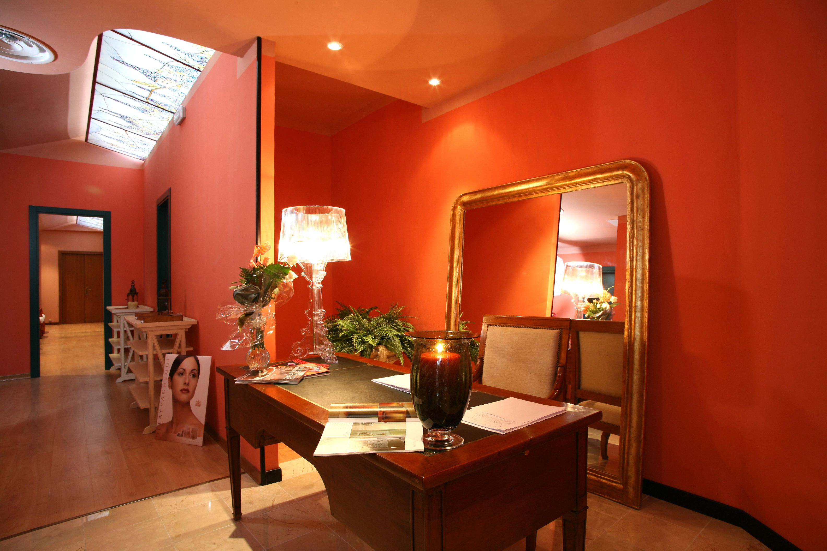 A hotel room with a wooden desk, a mirror, a lamp, and a vase.