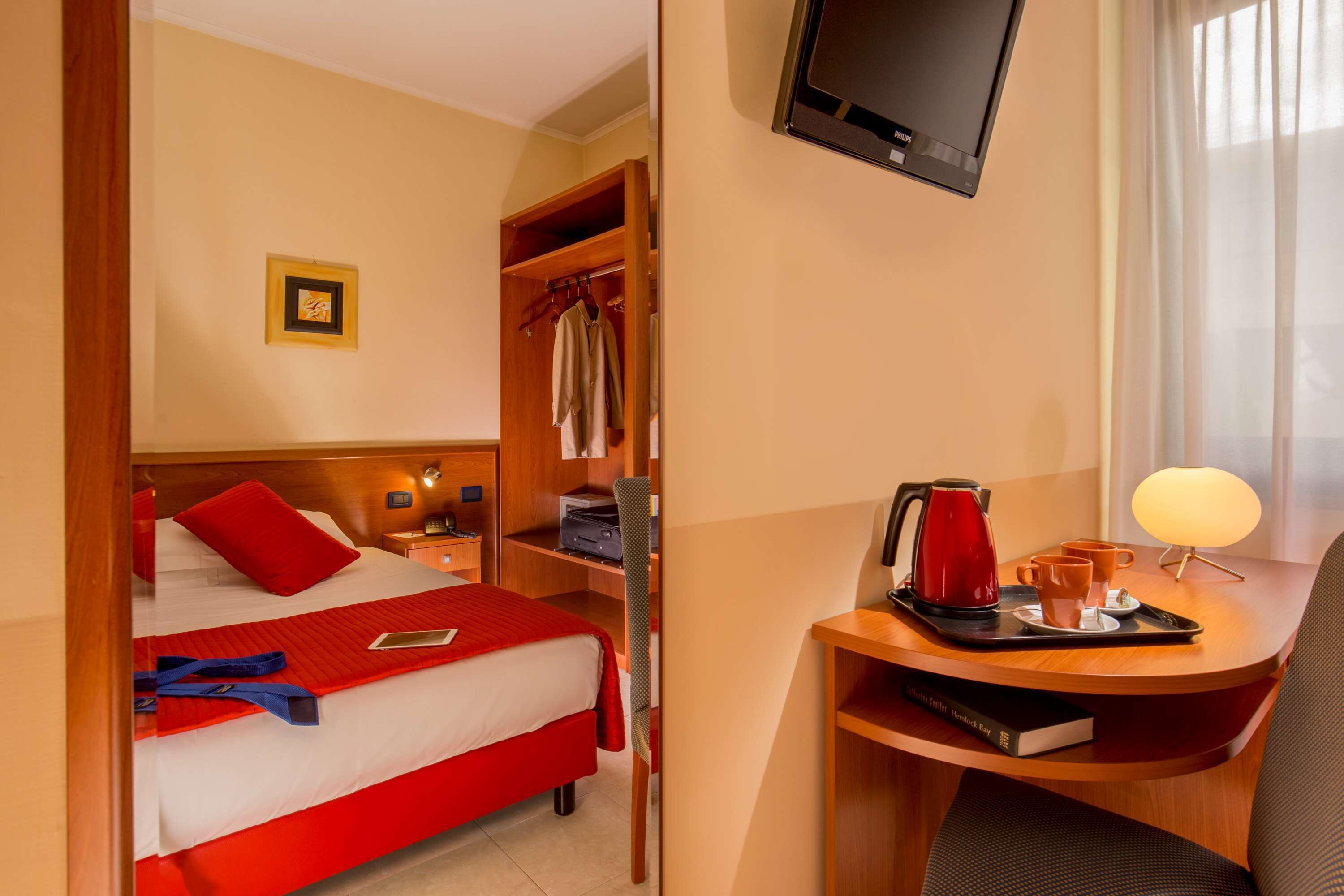 Une chambre d’hôtel avec un lit, un bureau avec une lampe, une télévision et une fenêtre avec des rideaux.
