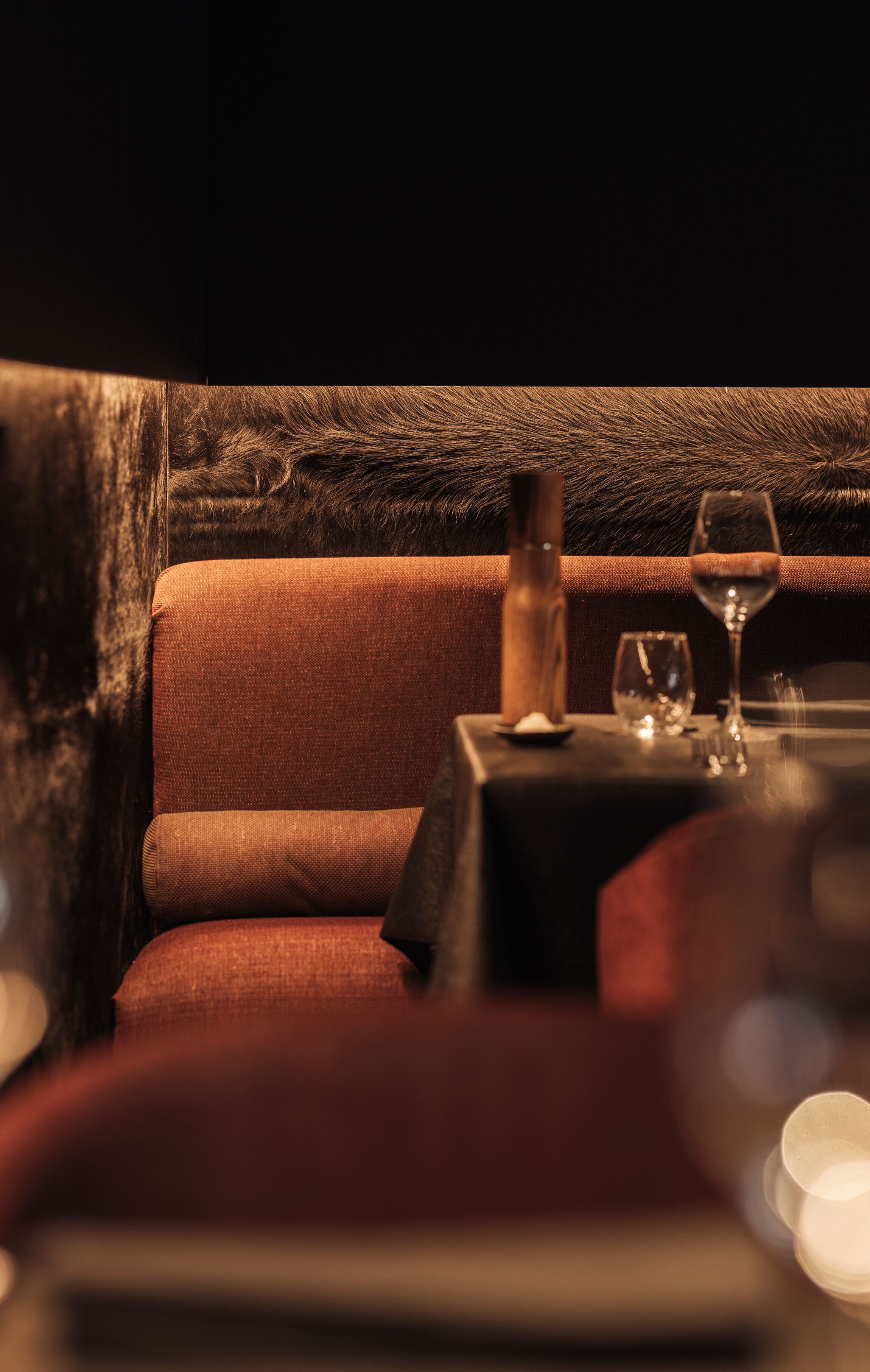 A dimly lit room with a plush red sofa, a small table with a wine glass and a candle, and a dark wooden accent wall.