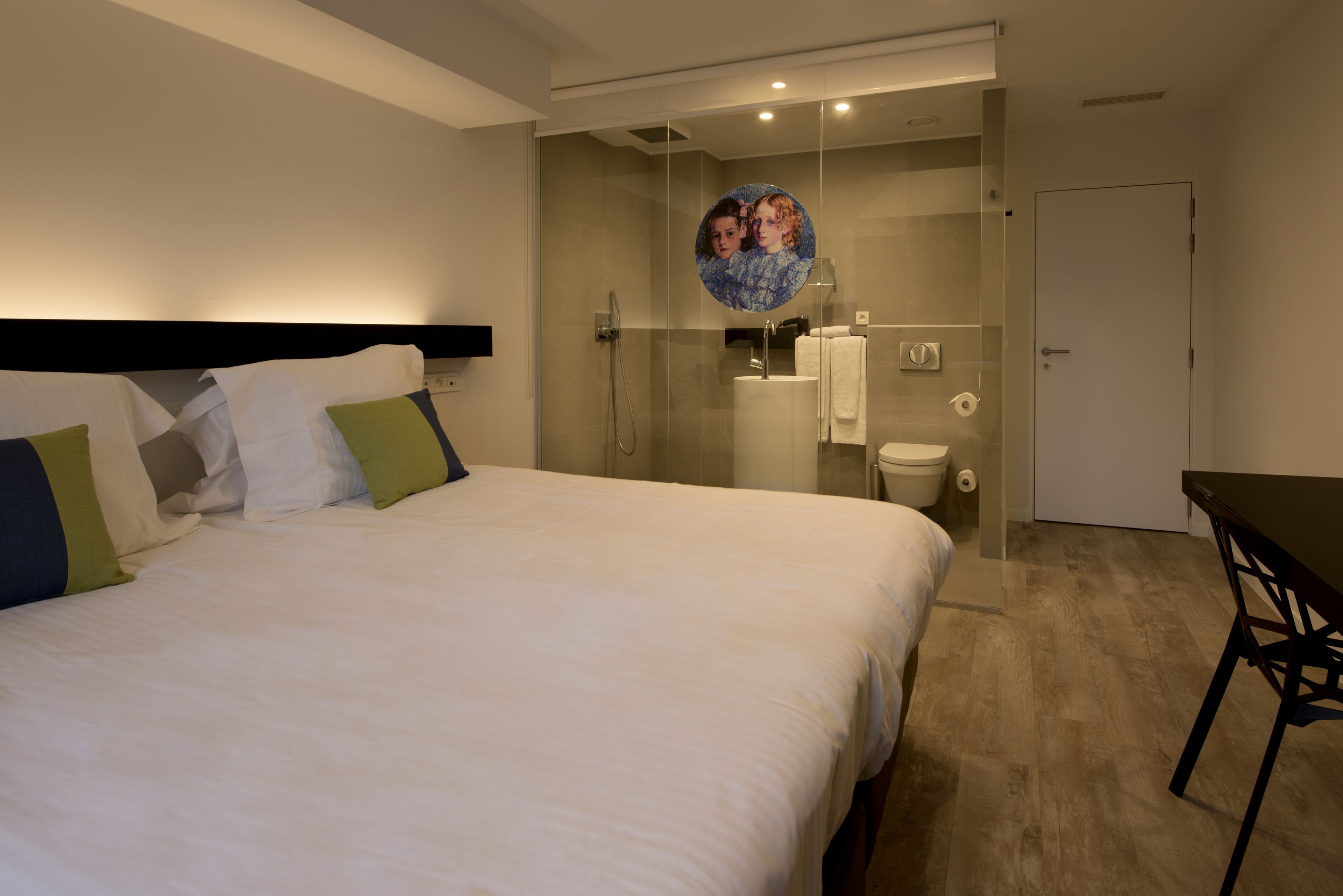 A hotel room with a bed, a desk, and a glass-enclosed shower area.