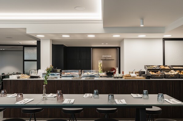 A modern breakfast bar with a variety of food options, a seating area with tables and chairs, and a clean, contemporary interior design.