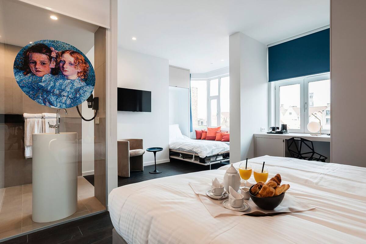 A modern hotel room with a bed, breakfast setup, a TV, and a window with a city view.