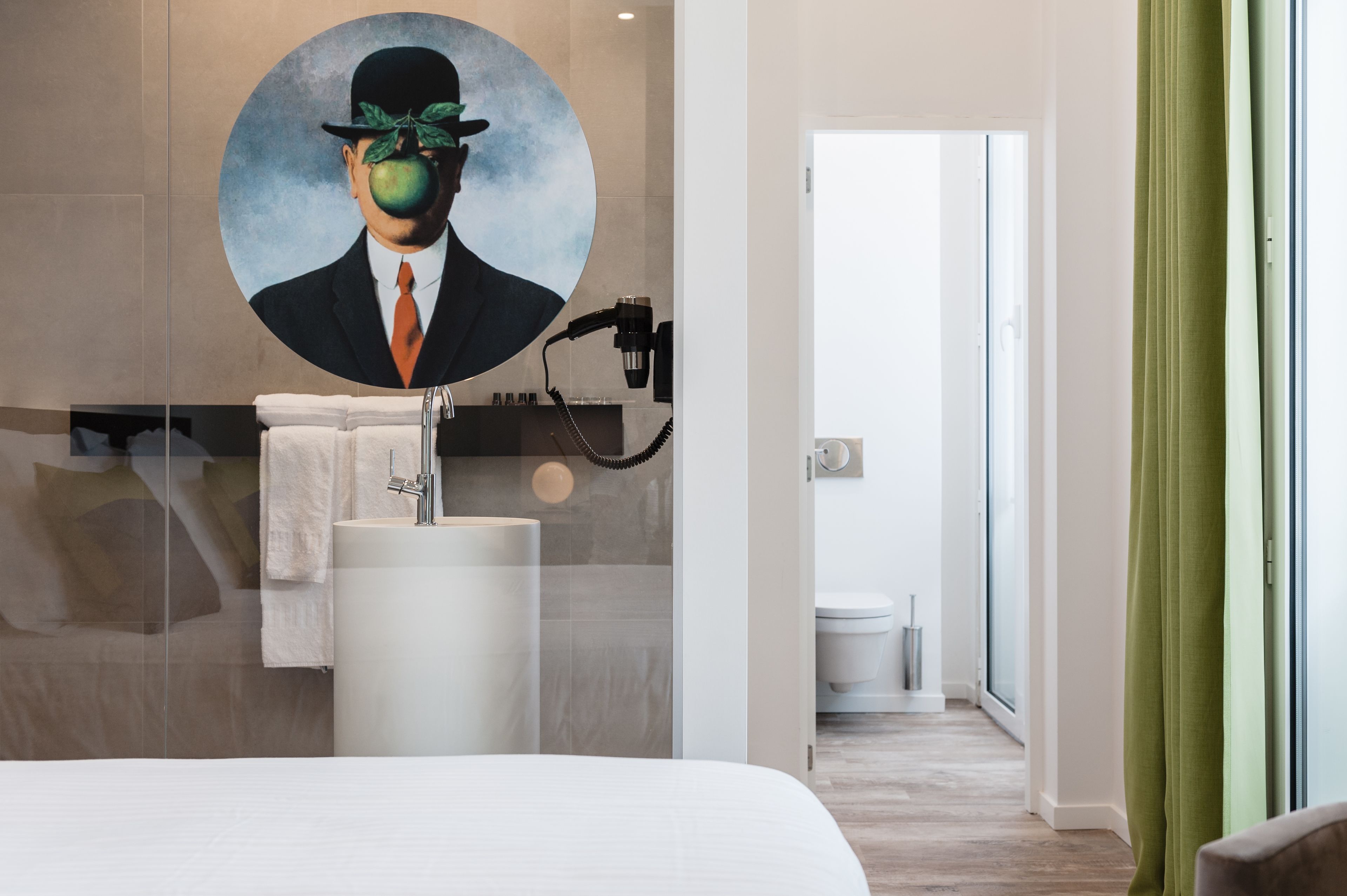 A modern bathroom with a large mirror, a sink, and a toilet. There is a painting on the wall above the mirror.