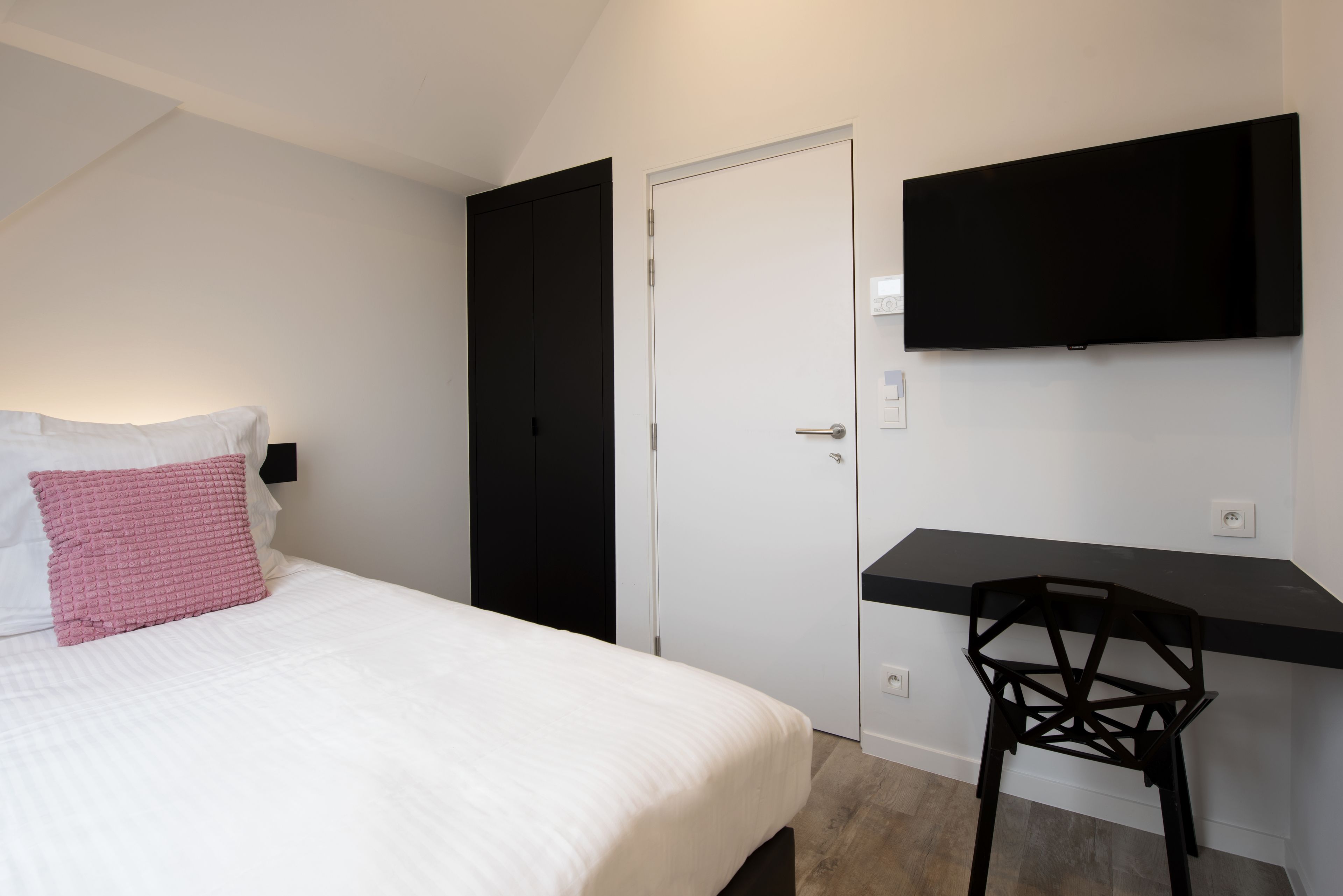 A bedroom with a bed, a desk, a chair, a TV, and a wardrobe.