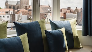 A window seat with cushions, overlooking a historic building with a tall tower. - Hotel Portinari (Bruges)