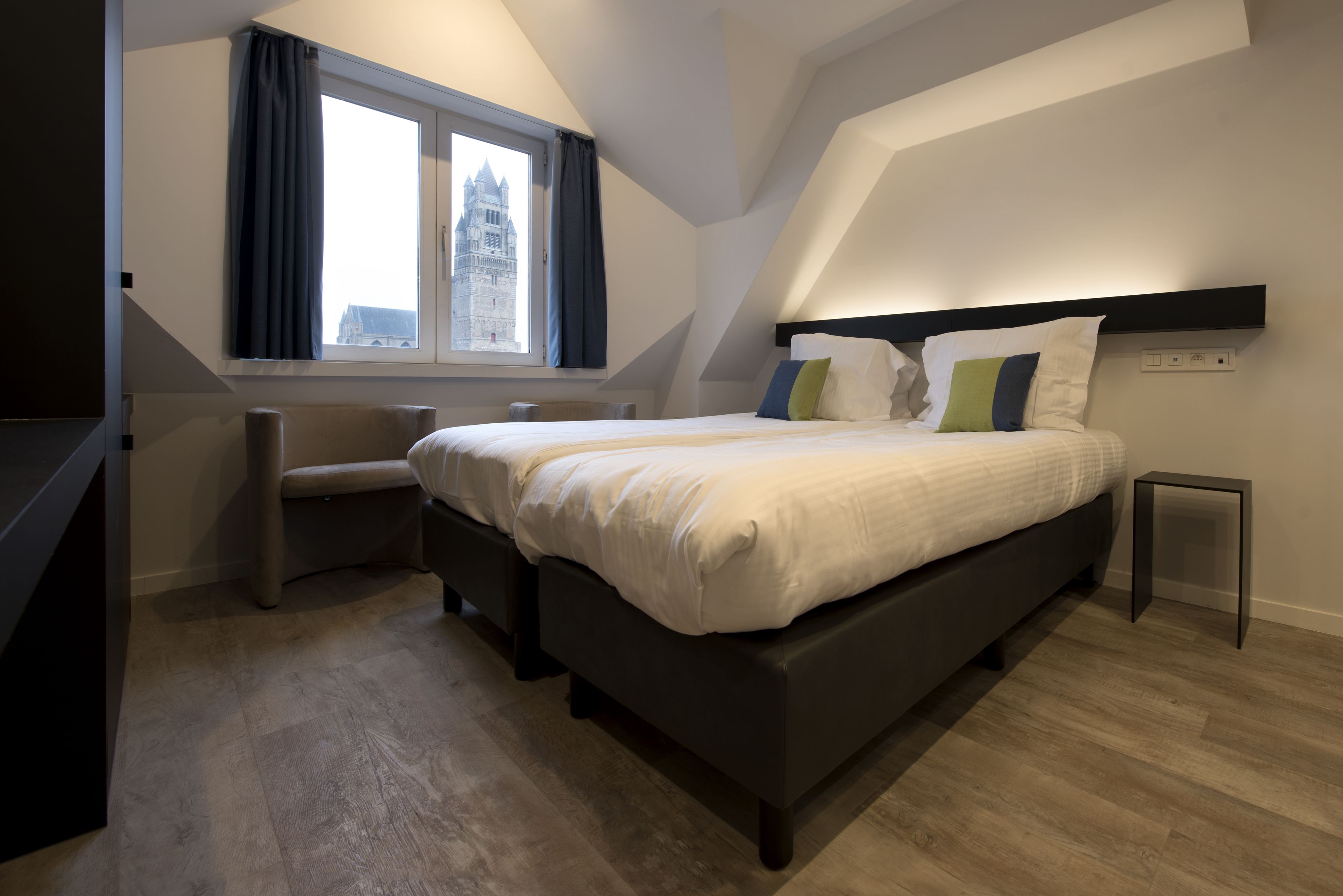 A modern bedroom with a large bed, a window with curtains, a view of a building, and a small table.