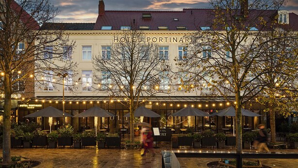 A hotel courtyard with outdoor seating, trees, and string lights. - Hotel Portinari (Bruges)