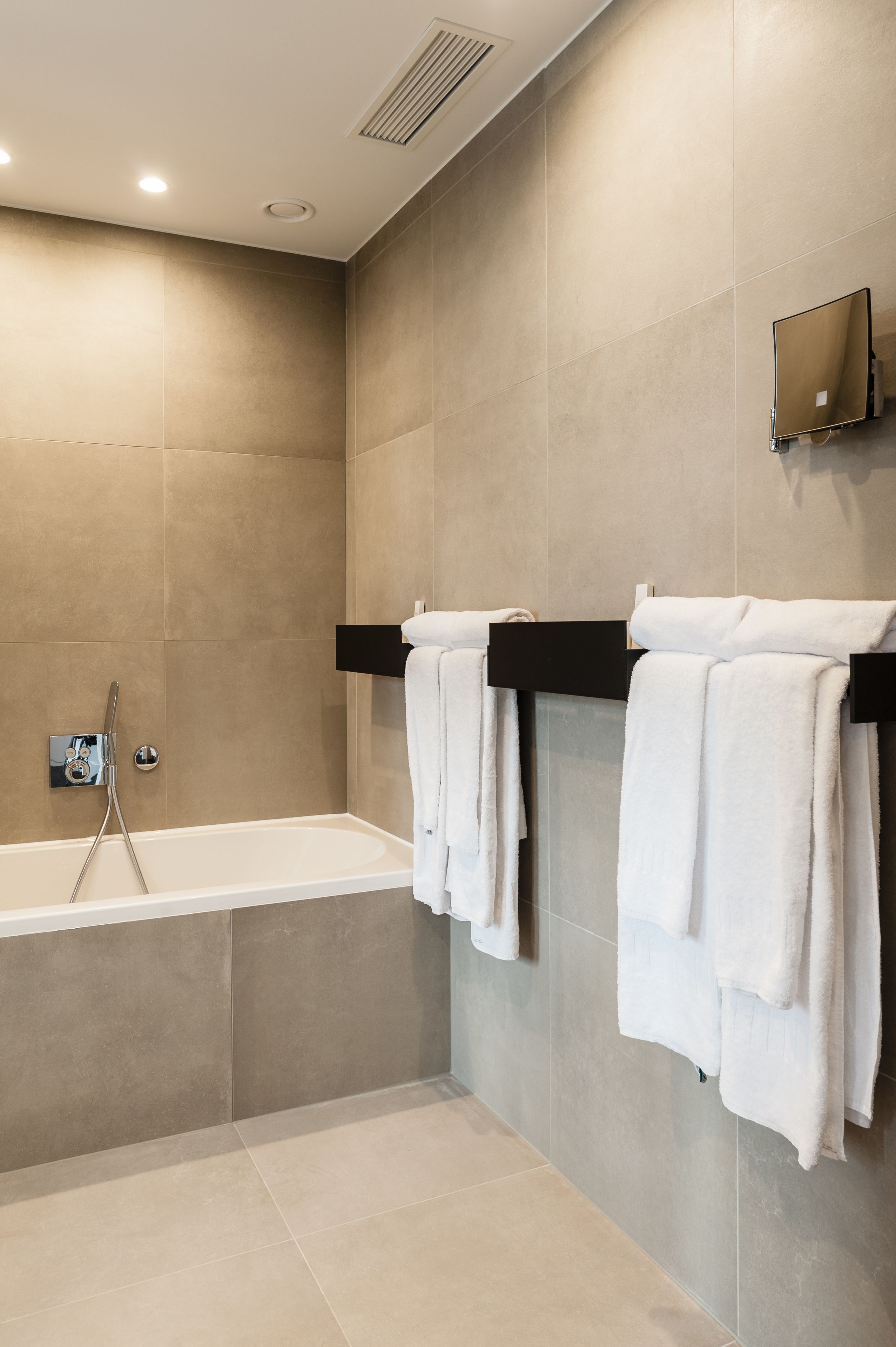 Une salle de bain moderne équipée d’une baignoire, d’une douche et d’un porte-serviettes avec des serviettes blanches.