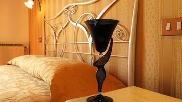 A hotel room with a bed, a bedside table with a black object on it, a wall-mounted light, and patterned wallpaper.