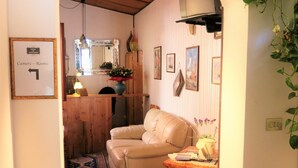 Un salon chaleureux avec un canapé beige, une table basse en bois et un tapis. Un couloir mène à une cuisine équipée de meubles en bois et agrémentée d’un miroir.