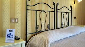 Une chambre d’hôtel avec un lit, une table de chevet sur laquelle est posé un panneau indiquant que le Wi-Fi est gratuit, et un luminaire fixé au mur.