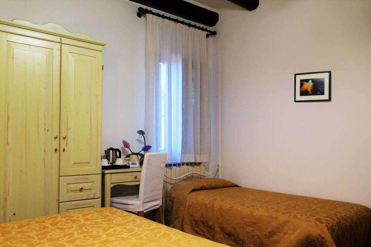 A bedroom with two beds, a desk with a chair, a wardrobe, and a window with curtains.