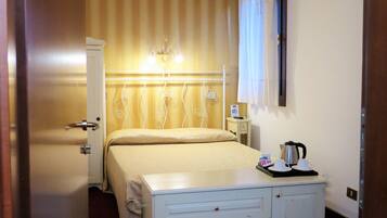 A hotel room with a bed, bedside table, lamp, and an air conditioning unit.