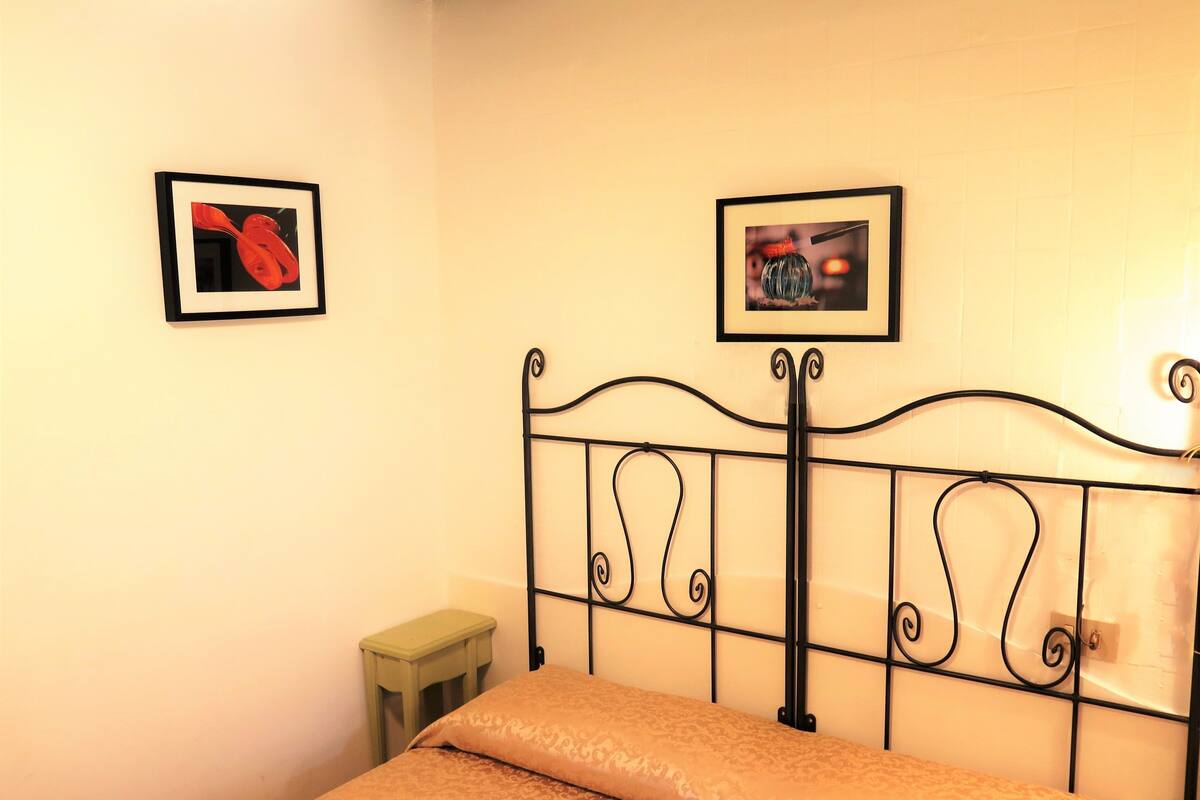 A bed with a metal headboard, a bedside table, and two framed pictures on the wall.