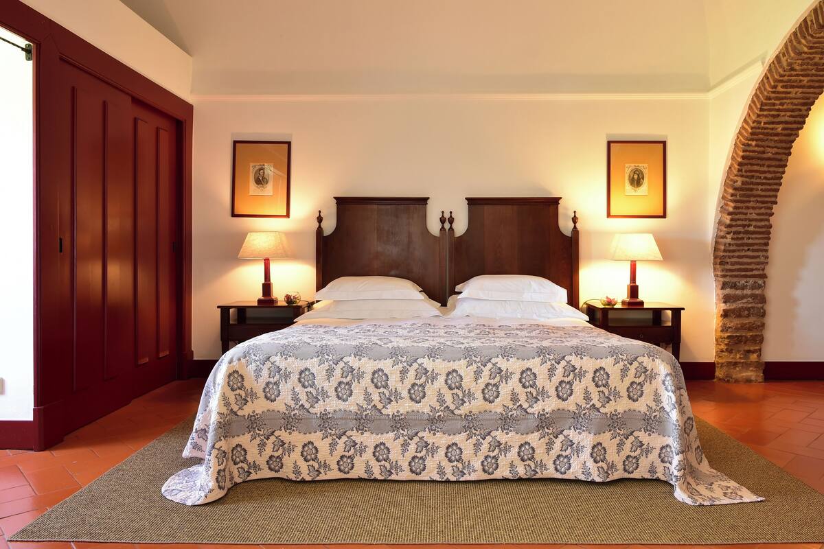 A bedroom with a large bed, two bedside tables with lamps, and a stone archway.